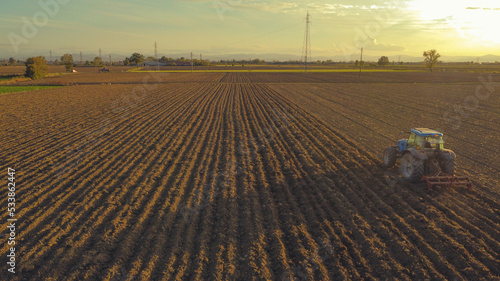 aerial view of farmer driving tractor deep plowing land at sunset, Piacenza, Italy  photo