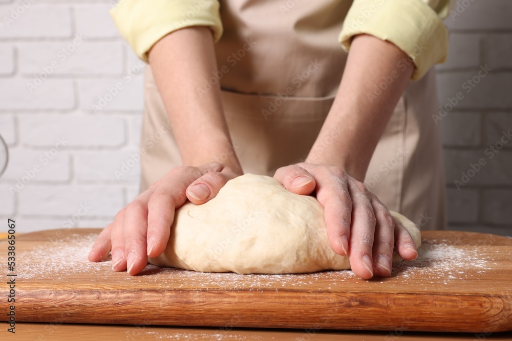 Woman kneading dough at wooden table near white brick wall, closeup