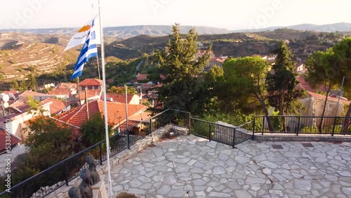 Aerial drone footage of traditional countryside hilltop village Vouni, in Limassol, Cyprus. Close up of greek and cypriot flags, Eoka monument and terracota ceramic tiled roof houses from above. photo