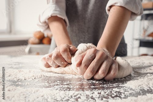 Woman kneading dough at table in kitchen, closeup