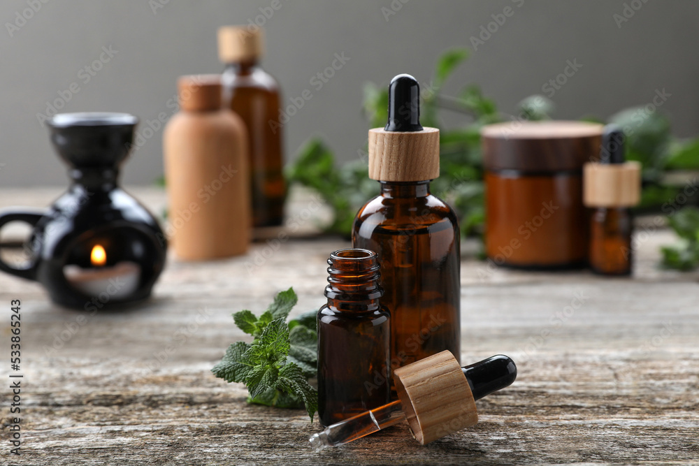 Bottles of mint essential oil and fresh leaves on wooden table Bottles of mint essential oil and fresh leaves on wooden table
