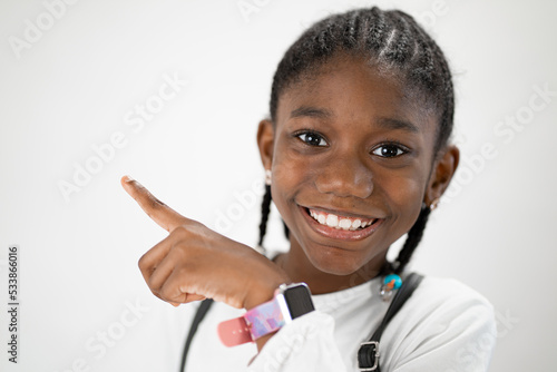 piccola ragazza nera isolata con sfondo bianco sorride alzando l'indice per indicare una direzione  photo