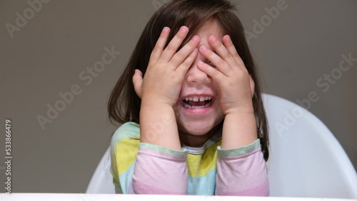 Cute happy girl closing her face and playing peekaboo or hide and seek with fun photo