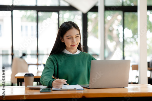 Asian woman working on laptop, female employee of a marketing company, she is working on a marketing plan for a company to generate income and profit, grow sales. Marketing planning concept.