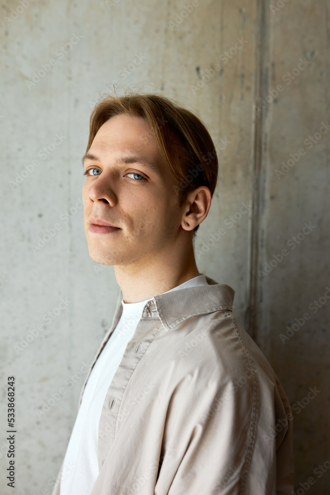 Portrait of confident young man looking at camera on gray textured wall dressed in beige shirt upon white t-shirt. Image of male manager in casual outfit posing on studio background Portrait of confident young man looking at camera on gray textured wall dressed in beige shirt upon white t-shirt. Image of male manager in casual outfit posing on studio background
