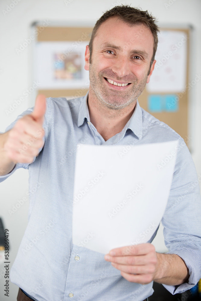 man in office holding paper and making thumbs up gesture Stock Photo