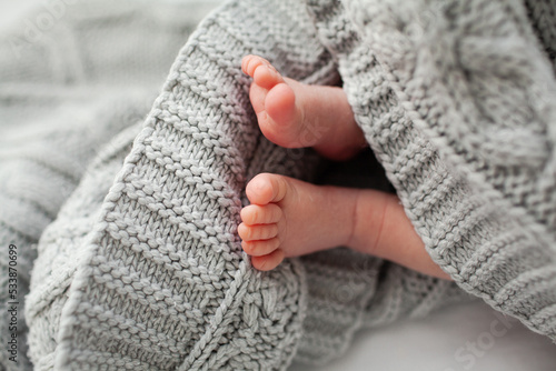 Close-up of the legs of a newborn lying in a crib with a white sheet and grey blanket
