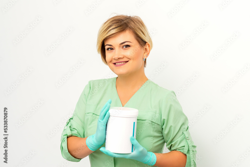 Cosmetics creams and skin care products in the hands of the female beautician smiling and standing over the white wall background Cosmetics creams and skin care products in the hands of the female beautician smiling and standing over the white wall background