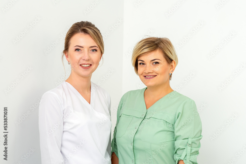 Close-up portrait of two young smiling female caucasian healthcare workers standing staring at the camera on white background Close-up portrait of two young smiling female caucasian healthcare workers standing staring at the camera on white background