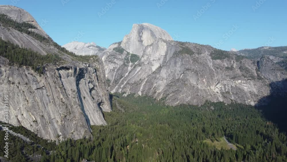 Yosemite National Park, drone aerial shot. Camera movement towards the left shows the iconic half dome and the granite monoliths. It shows also a cave on top of a mountain in front of the half dome. Yosemite National Park, drone aerial shot. Camera movement towards the left shows the iconic half dome and the granite monoliths. It shows also a cave on top of a mountain in front of the half dome.