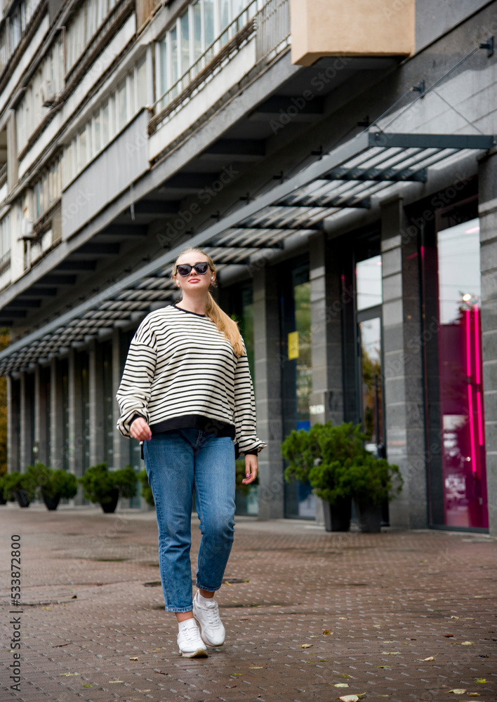 smiling woman with long blond hair in sunglasses and blue jeans walking on the street