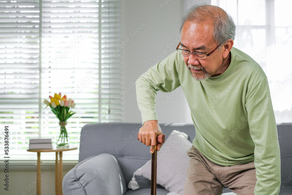elderly man using walking stick trying to stand and walk at home