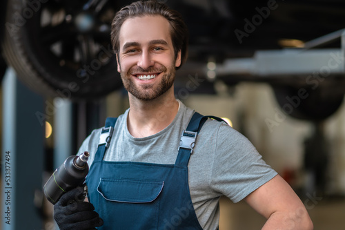 Joyful young car mechanic holding a work tool photo