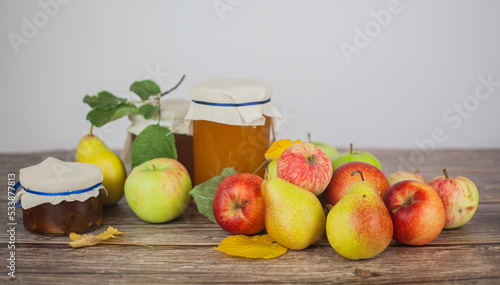 Ripe apples and pears and jars of apple jam on the table