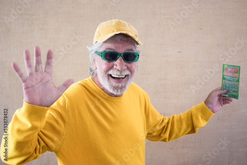 Happy caucasian senior man doesn't believe his eyes holding filled winning lottery ticket and celebrating victory. Lucky excited smiling mature man won a jackpot.