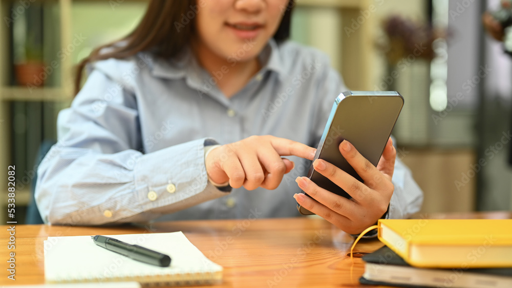 Cropped shot of smiling young woman typing typing text message on mobile phone while sitting at her office desk Cropped shot of smiling young woman typing typing text message on mobile phone while sitting at her office desk