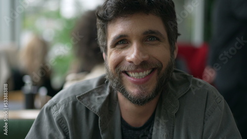 Portrait of a Brazilian young man sitting at coffee shop smiling at camera. Closeup 30s person face