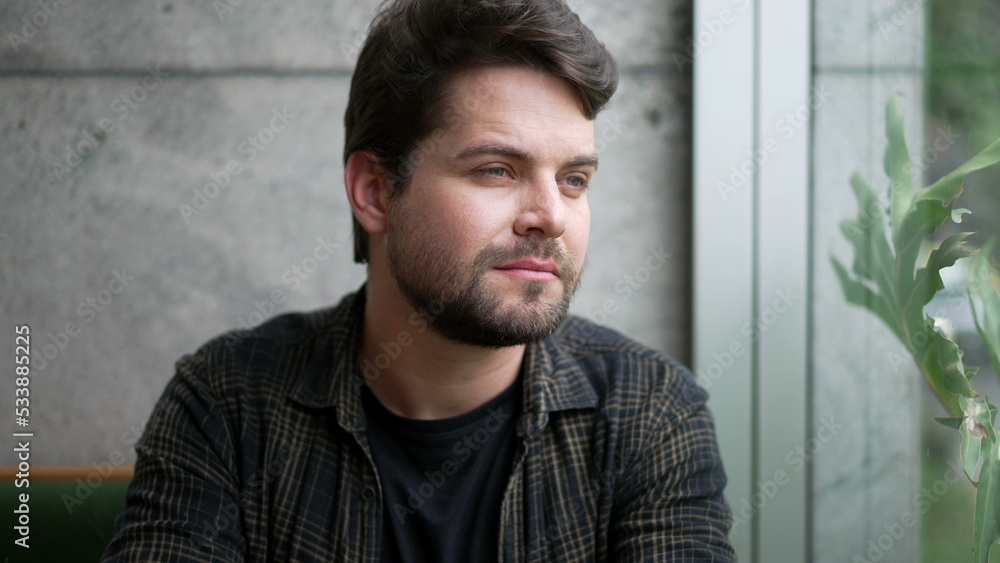 One pensive young man sitting by window looking at city. Thoughtful person closeup face pondering life One pensive young man sitting by window looking at city. Thoughtful person closeup face pondering life