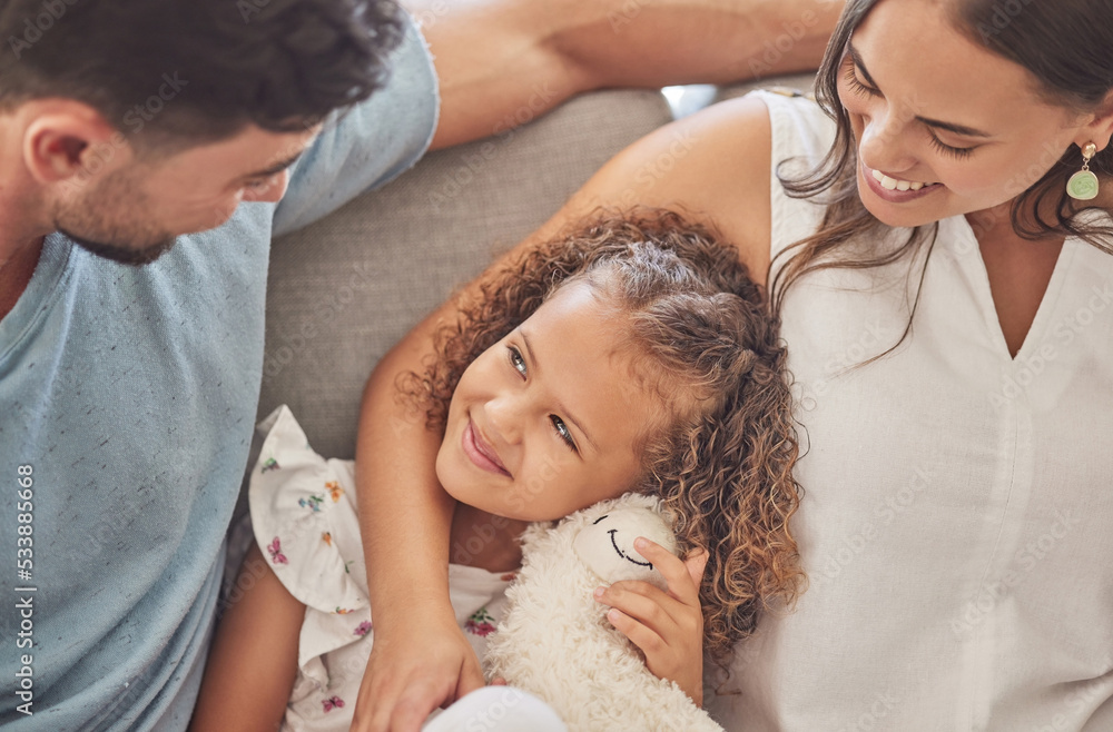 Fototapeta premium Love, family and girl bonding on a sofa with her parents, loving and caring in a living room at home. Happy, relax and smiling mother and father embracing their daughter, enjoy moment of parenthood