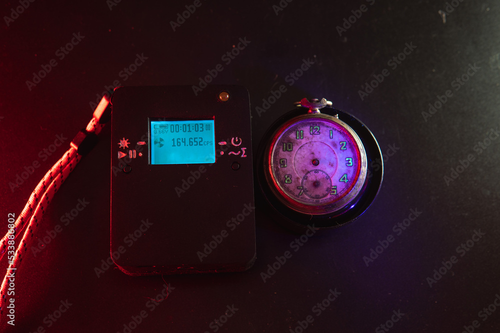 Dosimeter of radioactive radiation and old broken pocket watch with dangerous fluorescent paint