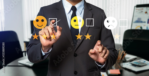 Customer service evaluation concept. Businessman pressing face smile emoticon show on virtual screen at tablet and smartphone in modern office.