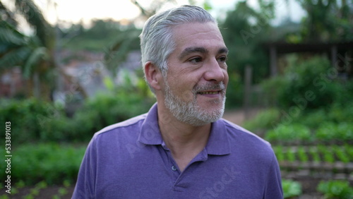 Contemplative senior man walking outdoors in small farm. Pensive older person walks forward portrait face closeup
