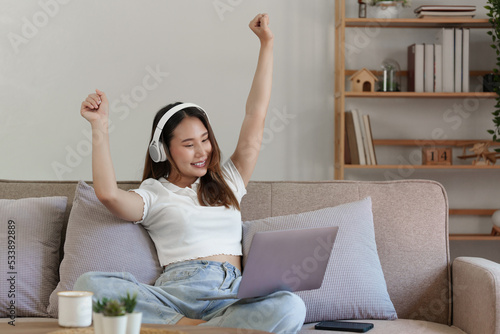 Attractive smiling young woman using laptop and listen music on sofa at home. lifestyle concept
