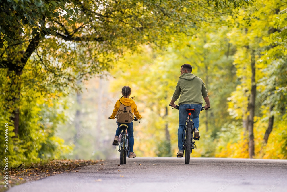 Obraz premium Happy father and daughter ride bicycles in autumn park on sunny day.