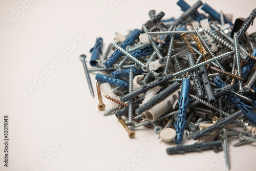 Close up isolated image of sets of grey plastic dowels plugs and shiny metal self-tapping screws in a heap, on white background.