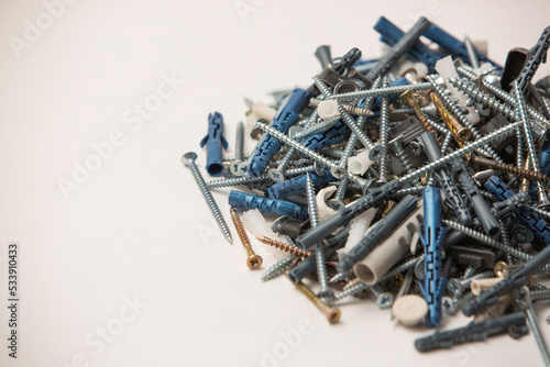 Close up isolated image of sets of grey plastic dowels plugs and shiny metal self-tapping screws in a heap, on white background.
