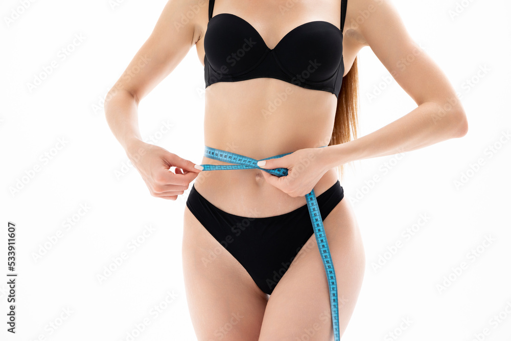 A slender girl in black lingerie measures her waist with a tape measure