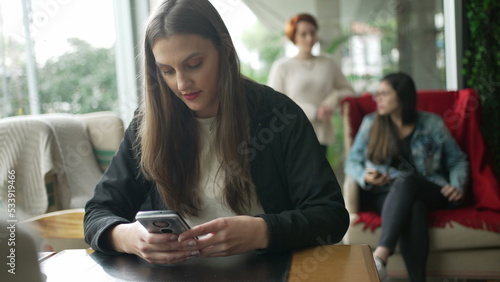 Young woman using phone sitting at coffee shop. Girl reading message on smartphone device at cafe restaurant place