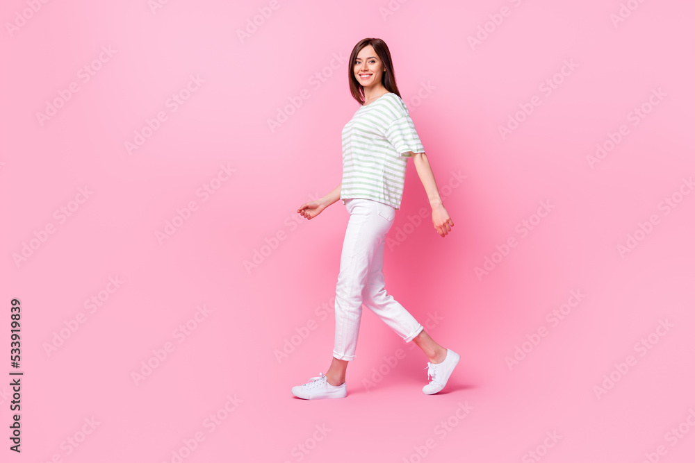 Full size photo of nice adorable gorgeous confident girl wear striped t-shirt white pants shoes walking isolated on pink color background