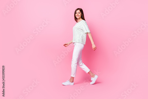 Full size photo of nice adorable gorgeous confident girl wear striped t-shirt white pants shoes walking isolated on pink color background