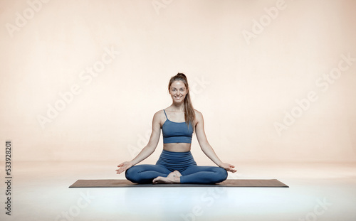 Smiling female yoga coach seated in lotus pose or Padmasana, meditate on mat. Women's health, healthy lifestyle