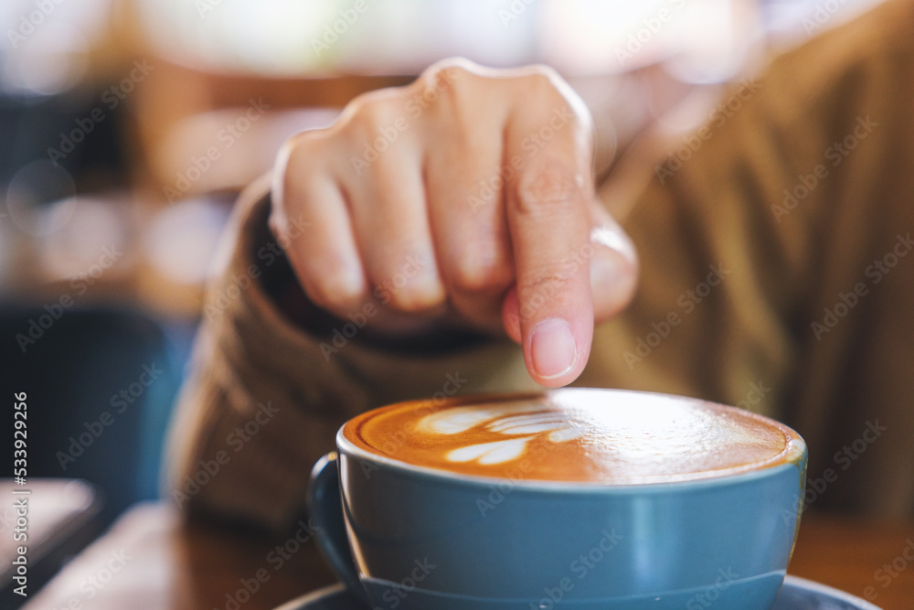 Closeup image of a hand pointing finger at a cup of hot coffee