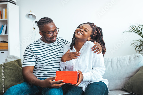 The guy gives a gift box to his girlfriend. Young couple on holiday. St. Valentine's Day. Smiling mid adult man surprising his girlfriend with a gift. Couple celebrating Valentines day anniversary