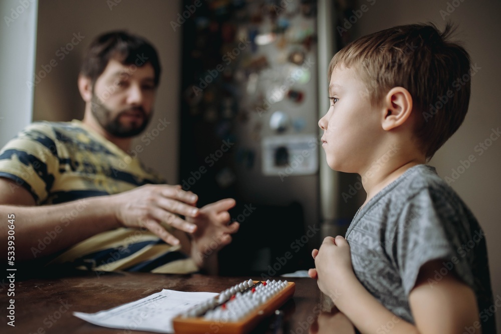 cute little caucasian boy doing his mental arithmetic homework with father sitting next to him at the kitchen table cute little caucasian boy doing his mental arithmetic homework with father sitting next to him at the kitchen table