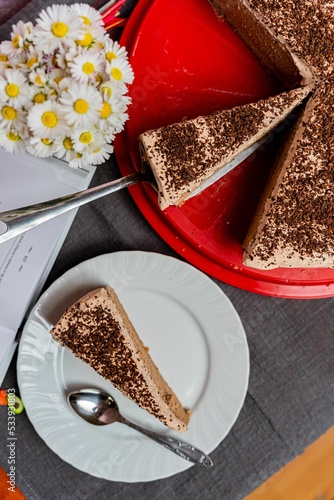 Vertical top view of sliced rum and chocolate cheesecake with a slice on a plate near flowers