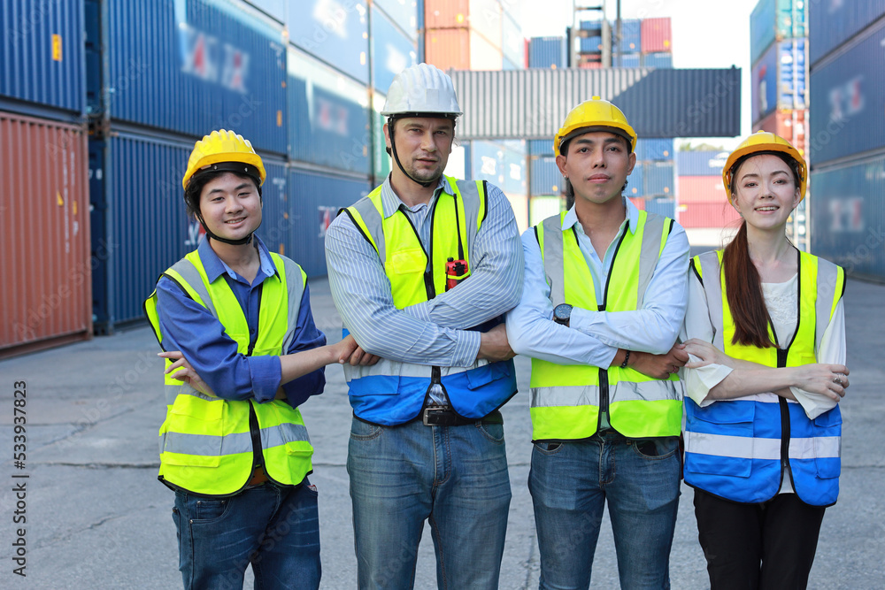 Group of multiethnic technician engineer and businessman in protective uniform with hardhat stand and crossed arms celebrate successful together or completed deal commitment at container cargo site Group of multiethnic technician engineer and businessman in protective uniform with hardhat stand and crossed arms celebrate successful together or completed deal commitment at container cargo site