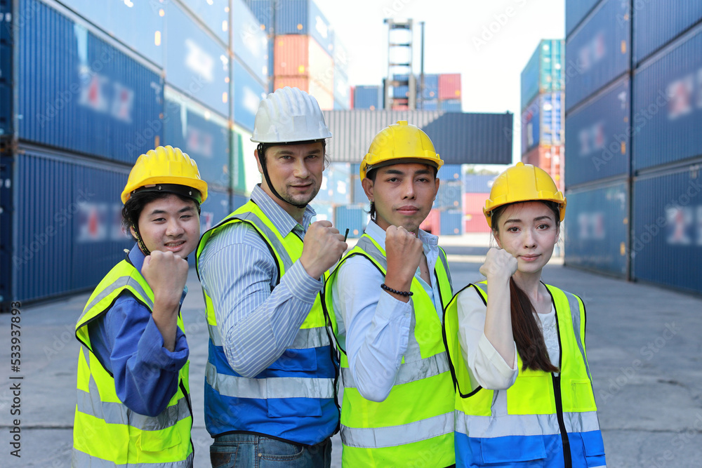 Group of multiethnic technician engineer and businessman in protective uniform with hardhat standing and raising hand celebrate successful together or completed deal commitment at container cargo site Group of multiethnic technician engineer and businessman in protective uniform with hardhat standing and raising hand celebrate successful together or completed deal commitment at container cargo site