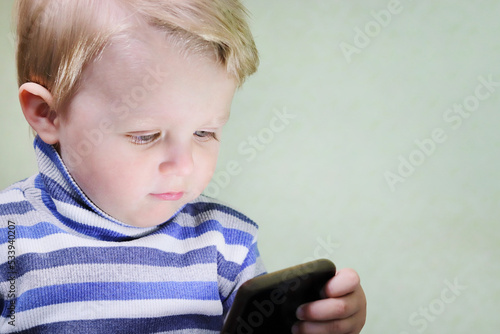 Defocused little inquisitive child holding a smartphone and looking at the screen. Children and gadgets. Copy space - technology concept, game on mobile device, watch cartoons online, communication