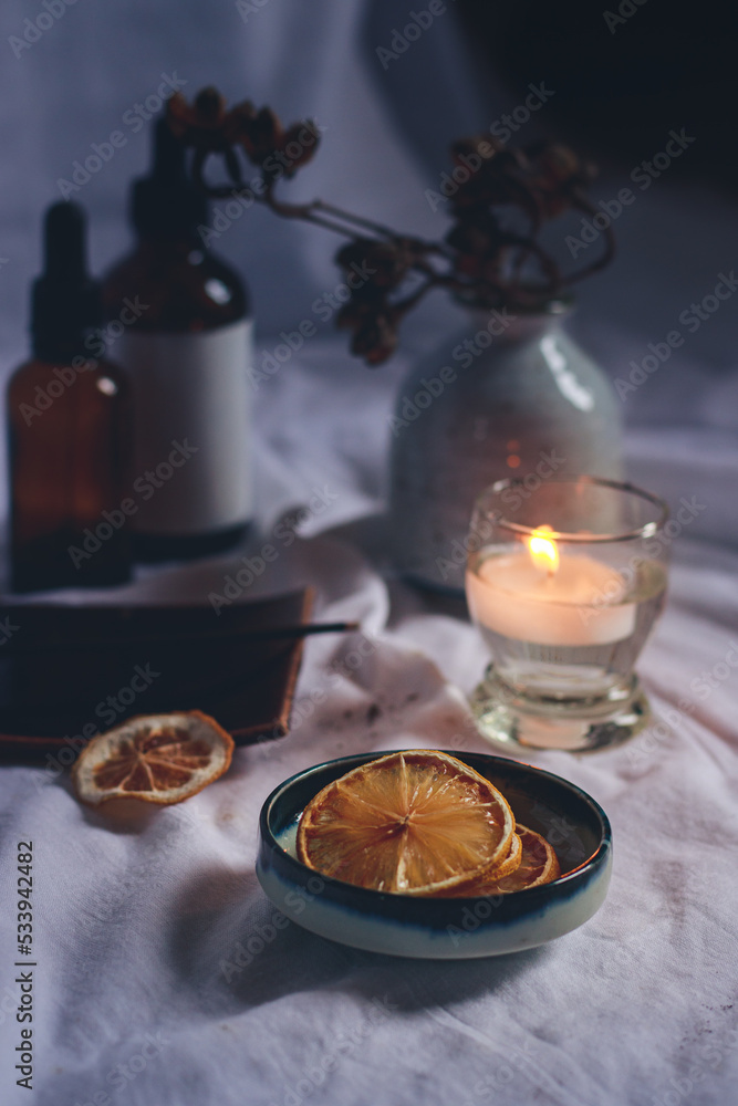 Vertical shot of essential oil bottles, dried lemon slices and a tea candle for a cozy autumn mood spa setting Vertical shot of essential oil bottles, dried lemon slices and a tea candle for a cozy autumn mood spa setting