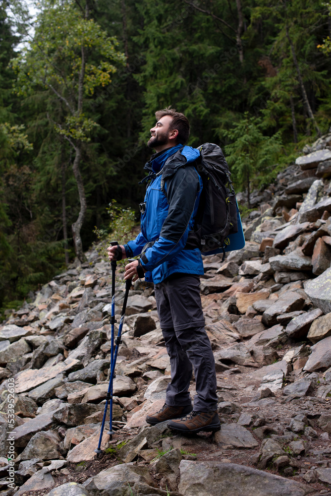 Happy hiker with trekking sticks enjoying view in rocky mountain forest. Resting and breathing. Full of stones. Activity and sport concept. Smile Happy hiker with trekking sticks enjoying view in rocky mountain forest. Resting and breathing. Full of stones. Activity and sport concept. Smile