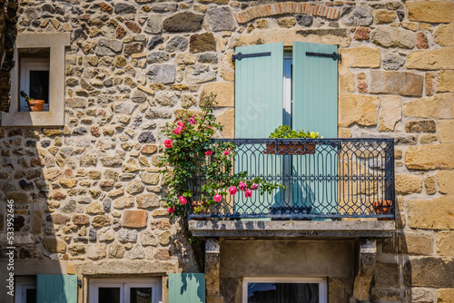 Obraz na plátně Facade of an old stone house, with flowery balcony and closed light shutters in