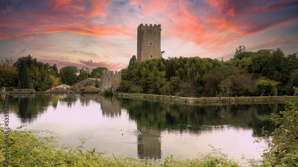 The castle and lake of the garden of Ninfa in Cisterna di Latina, Norma, near Rome Italy at sunset. Natural monument in Italy. The garden in English style. Romantic medieval knight view.