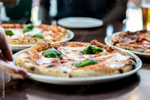 Close up view of a Margherita Neapolitan style pizza with buffalo mozzarella, tomato sauce and basil - Waiter hand serving pizza at pizza restaurant
