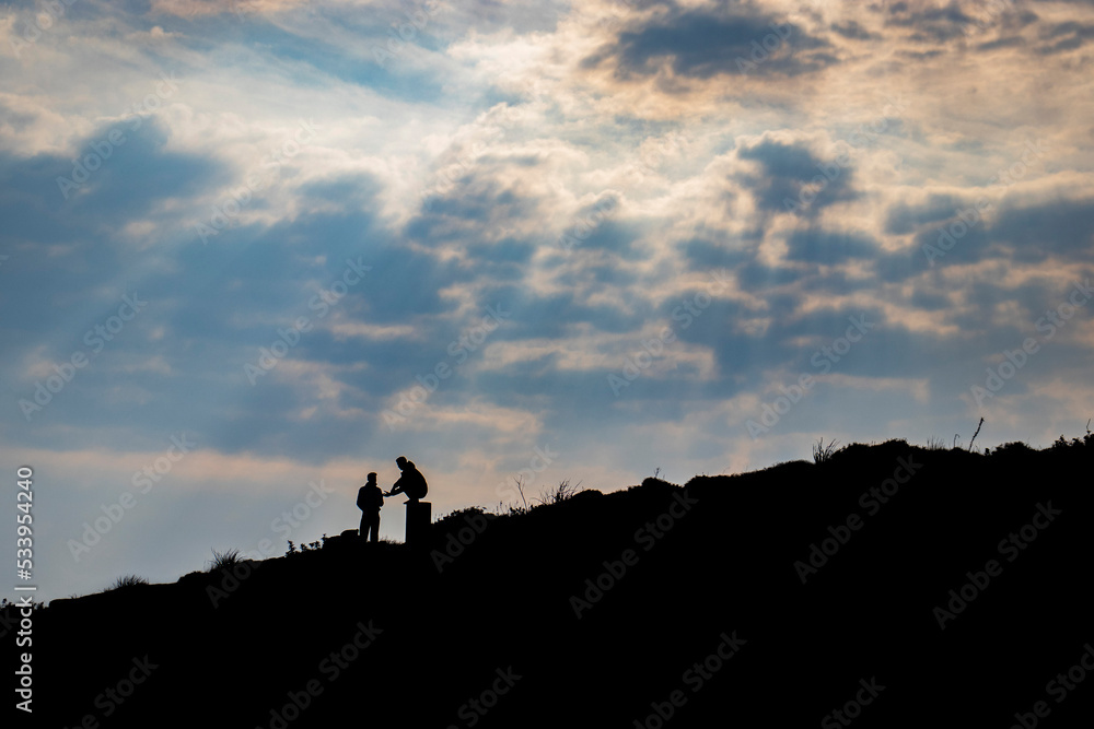 Mans silhouette standing in the hill under the clouds and sunlight halos.