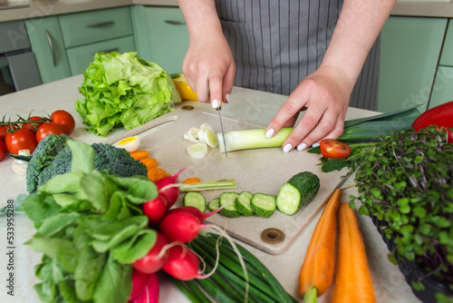 Woman cutting fresh vegetables for salad in kitchen