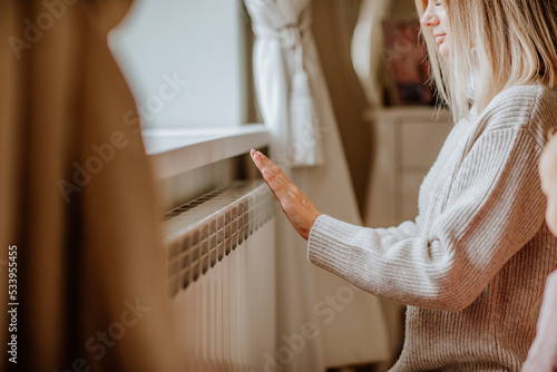 Young woman in long winter beige sweater is posing at home near the radiator photo